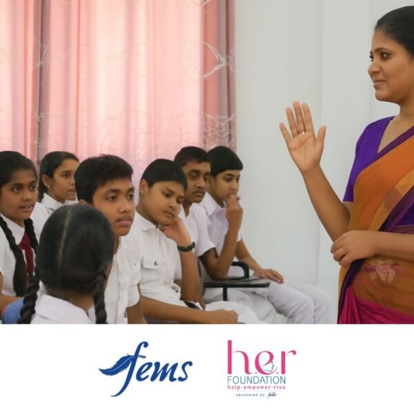 පිරිමි ප්රජාව | A female teacher wearing a purple and orange saree speaks to a group of Sri Lankan school students, both boys and girls, during an awareness session. Logos of Fems and the HER Foundation appear at the bottom, highlighting a menstrual health education program.
