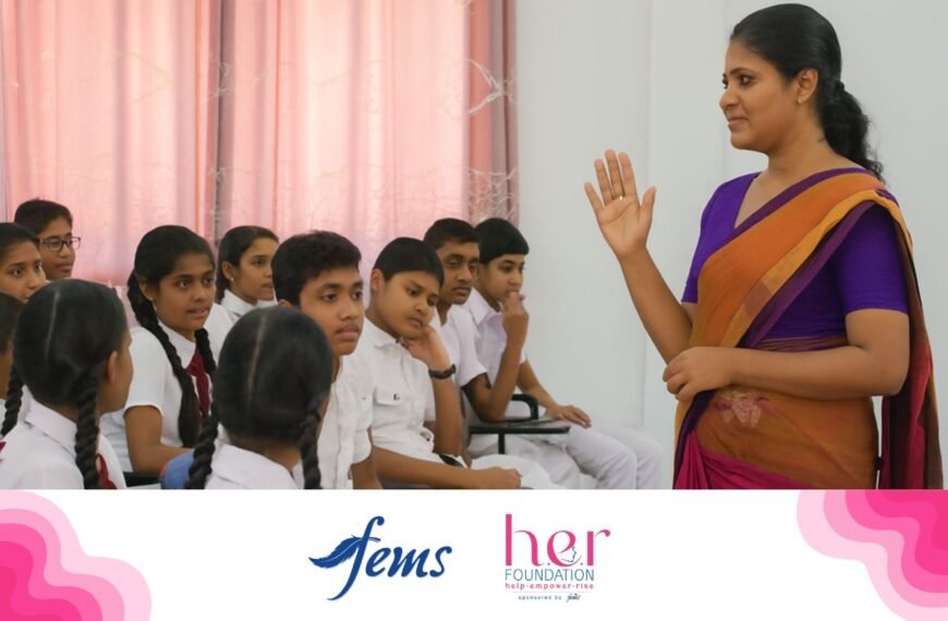 පිරිමි ප්‍රජාව | A female teacher wearing a purple and orange saree speaks to a group of Sri Lankan school students, both boys and girls, during an awareness session. Logos of Fems and the HER Foundation appear at the bottom, highlighting a menstrual health education program.