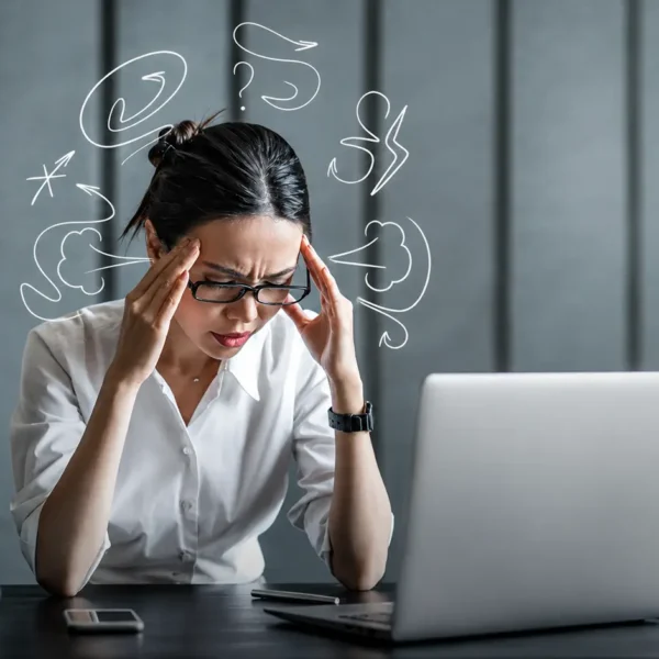 Perfect | Stressed professional woman holding her temples while working at a desk, illustrating perfectionism, overthinking, mental pressure, and workplace stress.