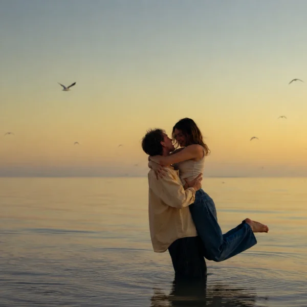 Marriage Goals | Romantic couple embracing in shallow water at sunset, with calm sea views, golden sky and birds flying in the background.