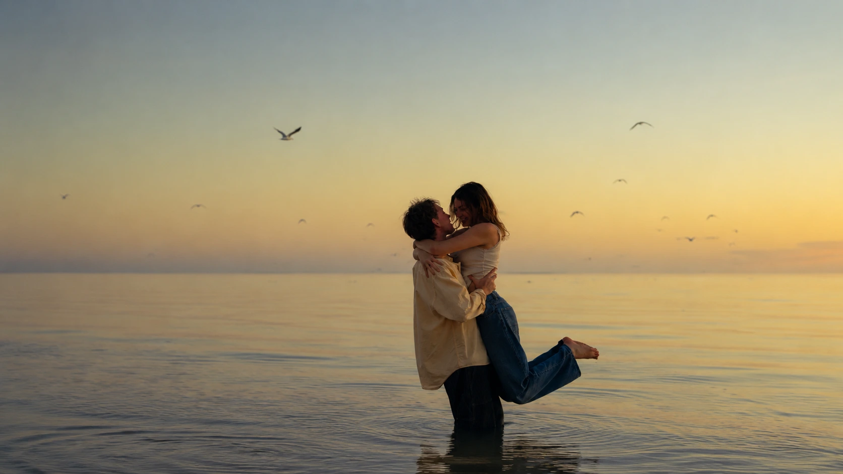 Marriage Goals | Romantic couple embracing in shallow water at sunset, with calm sea views, golden sky and birds flying in the background.