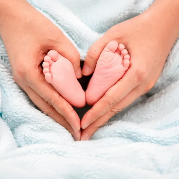Pregnancy | Adult hands gently holding newborn baby feet on a soft blue blanket.