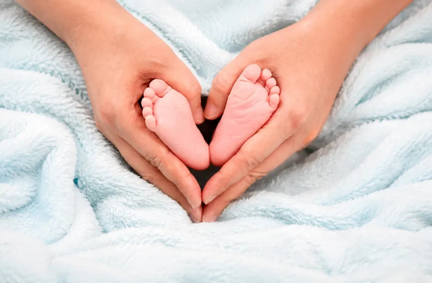 Pregnancy | Adult hands gently holding newborn baby feet on a soft blue blanket.